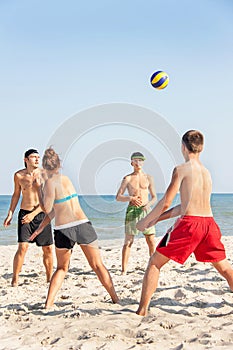 Teenages friends (four people) are playing volleyball on the beach.